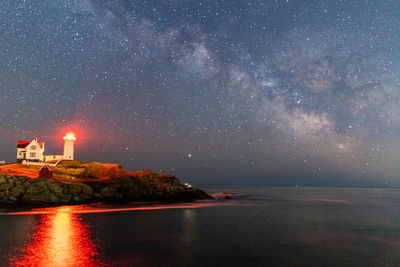 Milkyway stars shining above lighthouse and ocean along maine coast.