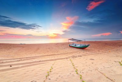 Boat moored on beach against sky during sunset