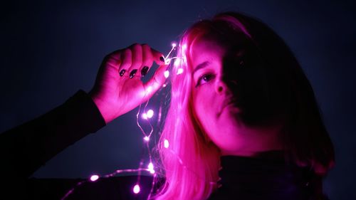 Portrait of young woman with pink hair against black background