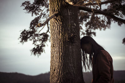 Androgynous person leans head on tree