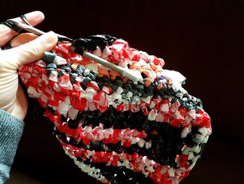 Close-up of hand holding knitting needles against black background