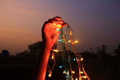 Close-up of hand holding illuminated light against sky during sunset