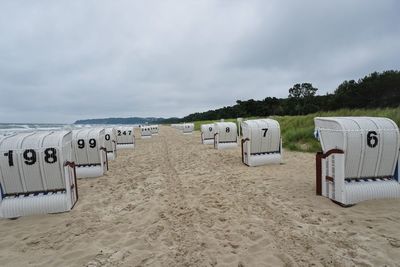 Hooded chairs on beach against sky