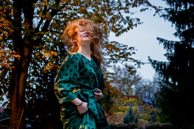 Portrait of young woman with tousled hair standing against trees