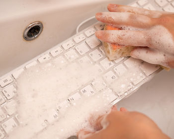 Woman washing white computer keyboard with a sponge with foam