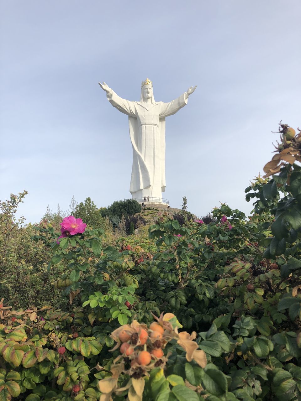 VIEW OF STATUE AGAINST PLANTS AND CROSS AGAINST SKY