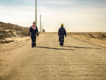 Rear view of men walking on road against sky