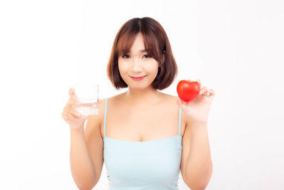 Portrait of smiling woman drinking glass against white background