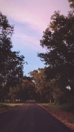 Road amidst trees against sky during sunset