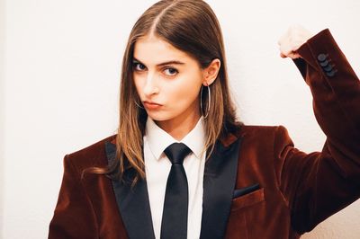 Portrait of young woman flexing muscles while standing against white background