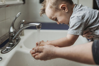Side view of young toddler having hands washed in sink by dad