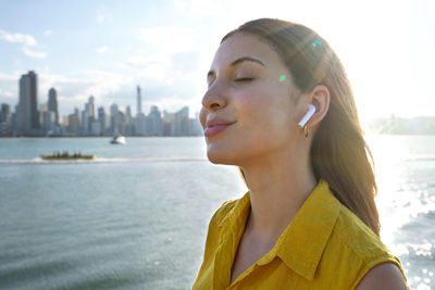 Woman listening relaxing music with earphones breathing with skyscrapers in the city bay on sunset