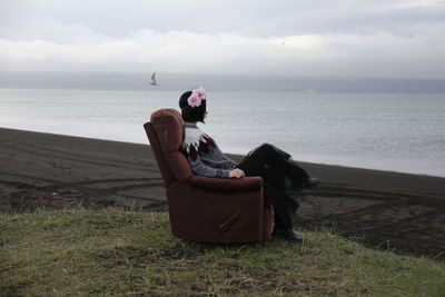 Side view of woman sitting on armchair on field against sky