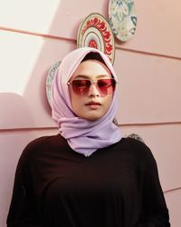 Young woman wearing sunglasses and headscarf against wall