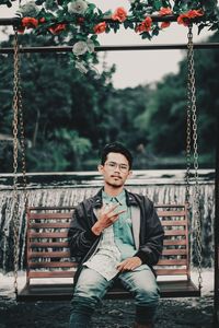 Portrait of young man sitting on swing at park