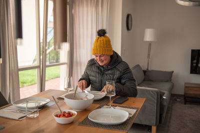 A woman sits at the dining table, dressed warmly, and eats