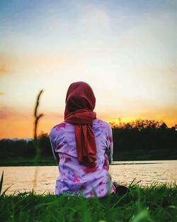 Rear view of woman by lake against sky during sunset