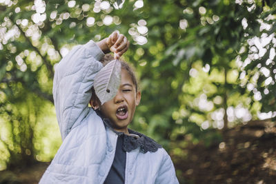 Playful girl making face while looking through hole in dry leaf