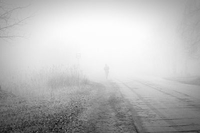 Rear view of man walking on snow covered landscape in foggy weather