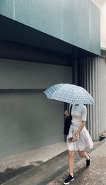 Full length of woman holding umbrella walking on street