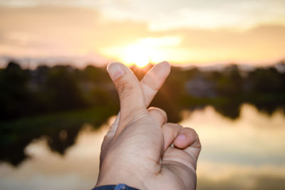 Close-up of person hand against sky during sunset