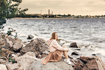 Woman sitting on rock by sea against sky