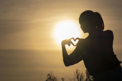 Silhouette man holding camera against sky during sunset