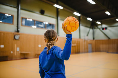 Rear view of girl holding handball in sports court