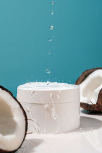 Two halves of coconut and a jar of cosmetics on a blue background with water drops.