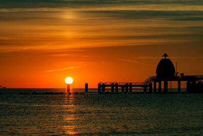 Silhouette built structure by sea against orange sky