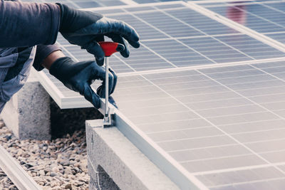 Unrecognizable male mechanic in protective gloves using screwdriver and installing solar panels on roof of building