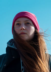 Young woman long hair in pink hat black coat blue sky background. stylish millennial girl walking