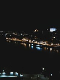 Illuminated buildings by river against sky at night