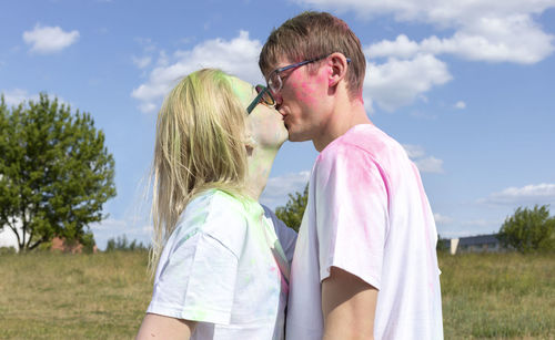 Romantic caucasian couple adults kiss with colorful paint, powder on clothes on holi color festival