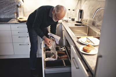 Senior man throwing unpacked box in dustbin at home
