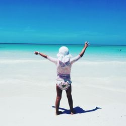 Full length rear view of girl standing at beach against sky