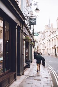 Rear view of man walking on street amidst buildings in city