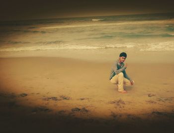 Boy standing on beach against sky during sunset