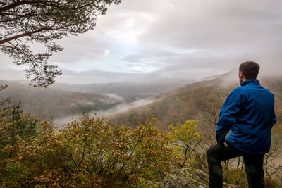 Rear view of hiker standing on mountain against sky during sunset