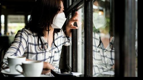 A woman wearing a medical mask sits in a cafe looking out the window.