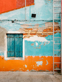 Ancient facade of dwelling with ruined orange and blue plaster