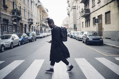 Fashionable man using mobile phone while crossing road in city