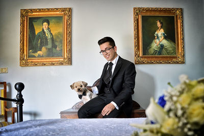 Portrait of bridegroom with puppy sitting on table at home