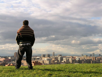 Rear view of man with cityscape against cloudy sky