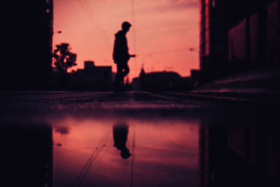 Reflection of silhouette man on puddle at sunset