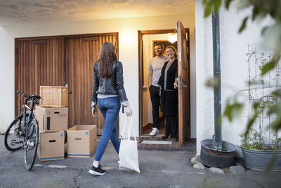 Parents looking at daughter walking by cardboard boxes and bicycle outside house