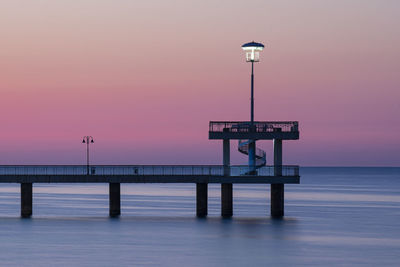 Street light by sea against sky at sunset