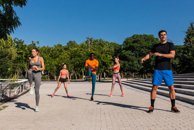 Group of multiethnic sportspeople stretching bodies while warming up before workout in city