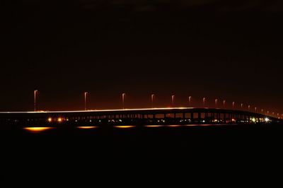 Illuminated bridge over river against sky at night