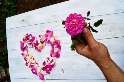 Cropped image of person holding flower against heart shape on table